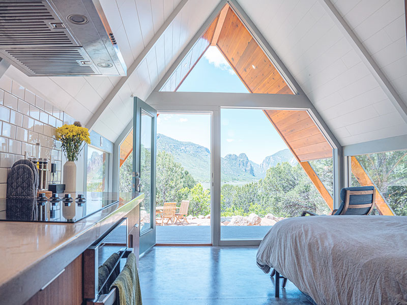 A bedroom with a wooden ceiling looking out over a beautiful green landscape of mountains and trees