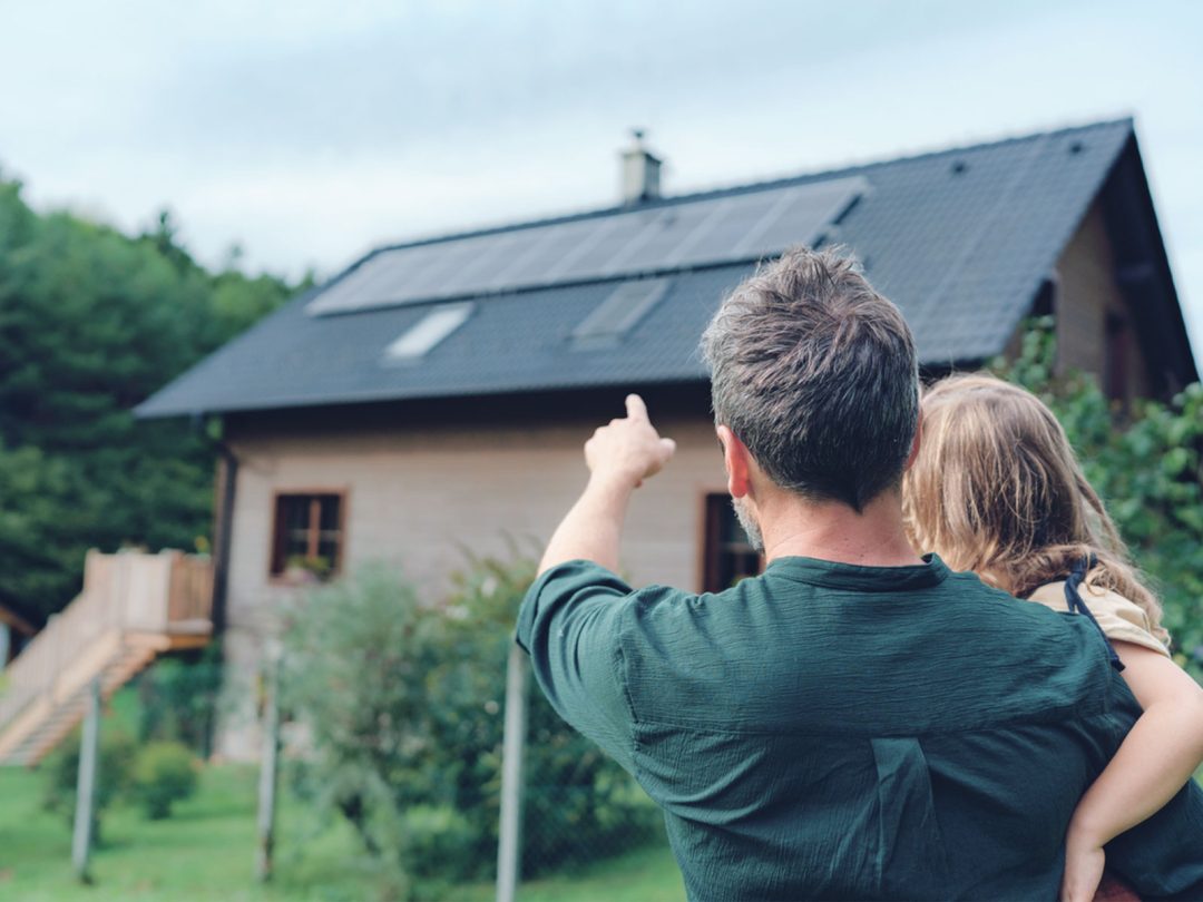 A father holding his daughter pointing at a home with solar panels stuck to the roof