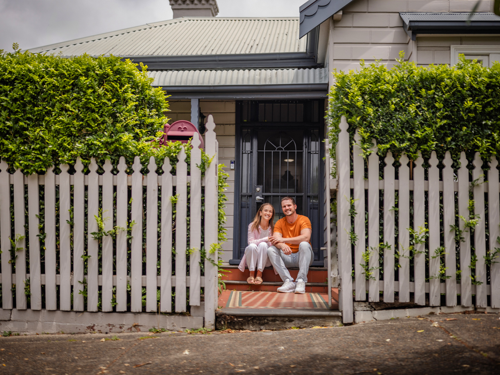 A young couple sitting at the doorstep in front of their new house