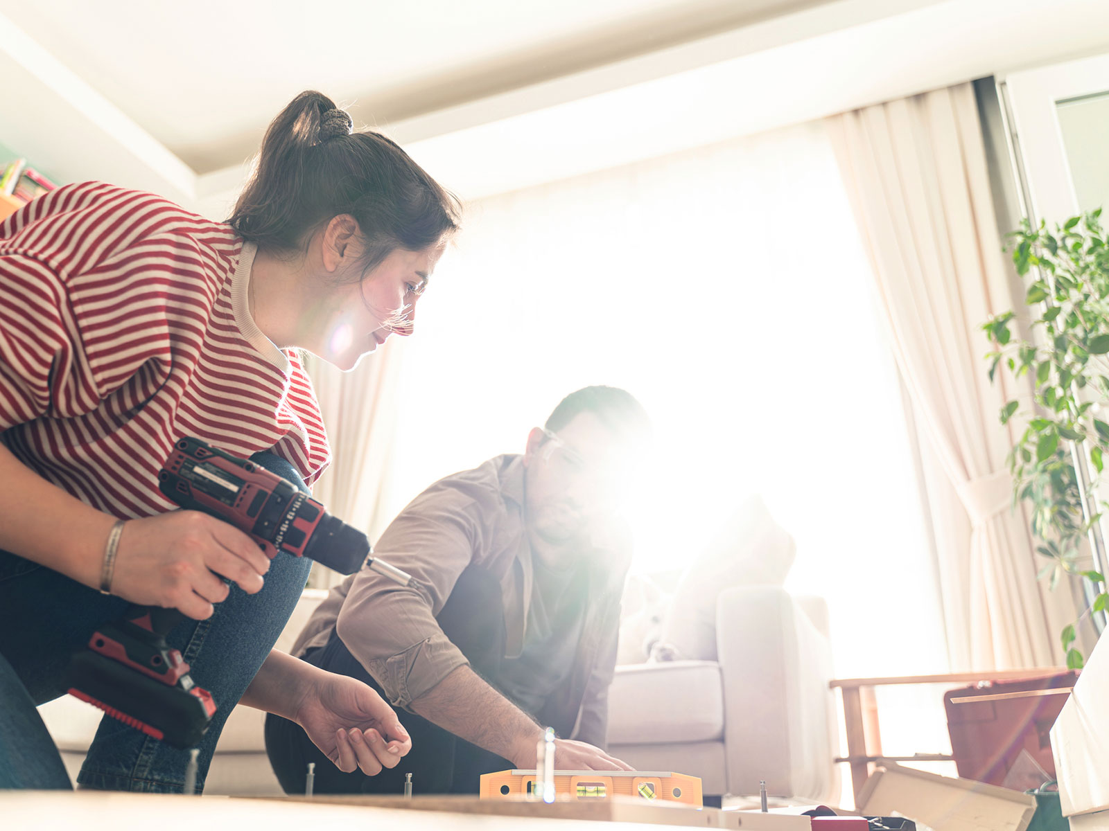Young couple with screwdriver and tools in hand assembling a piece of new furniture in their home