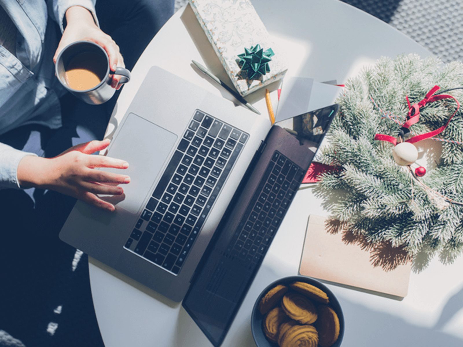 Hands working on laptop, with Christmas wreath and present nearby.